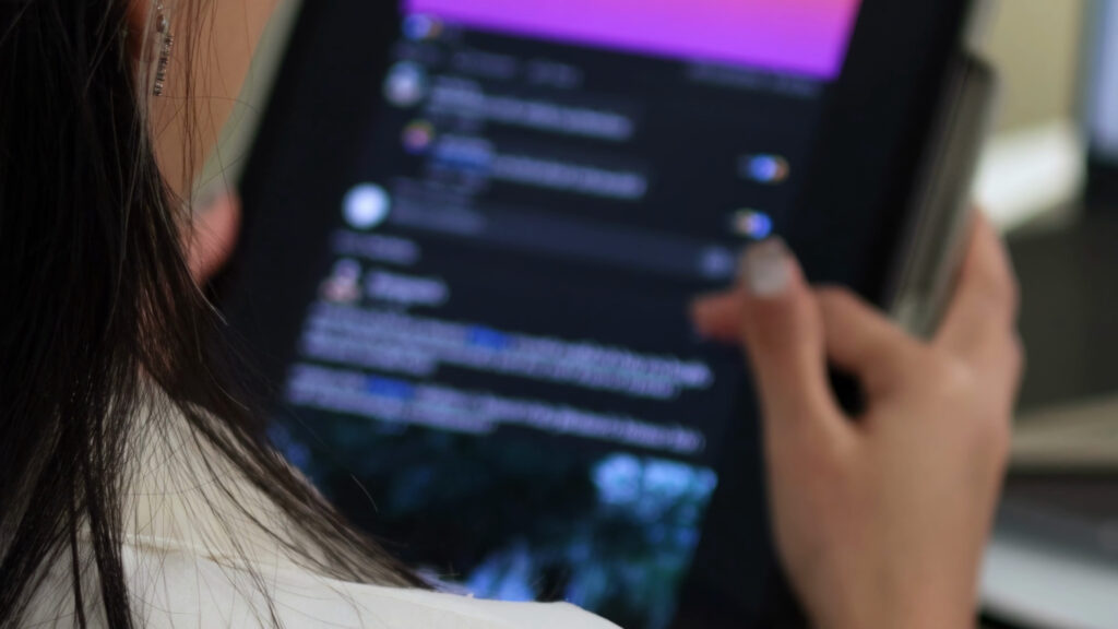 Close-up of a person holding a smartphone; the screen shows blurred, code-like text on a dark background.
