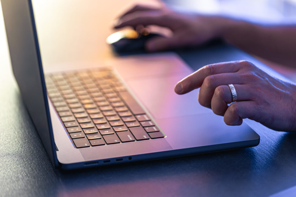Person typing on a laptop with one hand on the keyboard and the other on a mouse nearby.